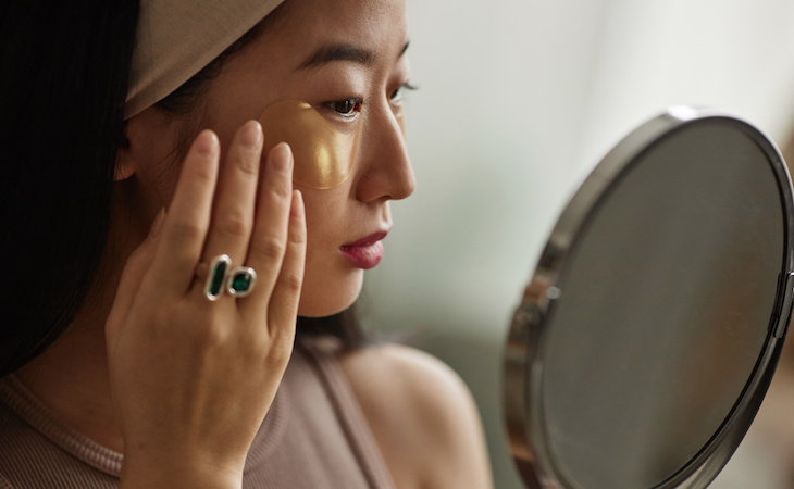 persona applying under-eye patches and looking in mirror