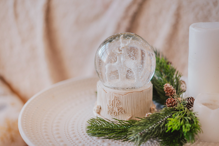 Magic glass snow globe with deer and spruce branches on the bedside table in a light interior