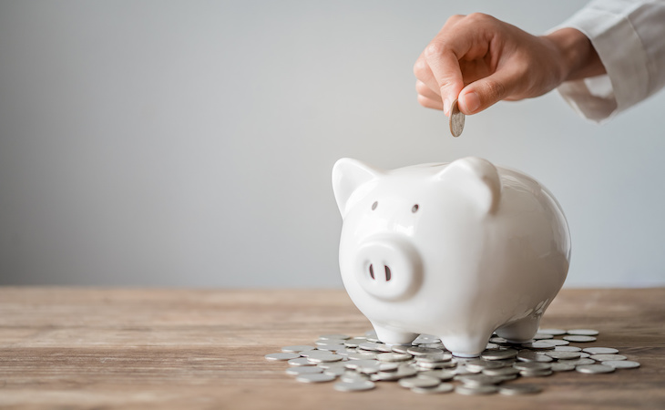Hand holding coin going into piggy bank