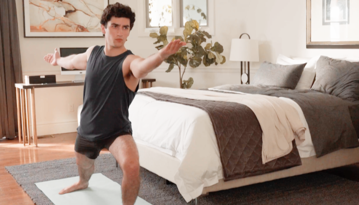 man practicing yoga in front of bed