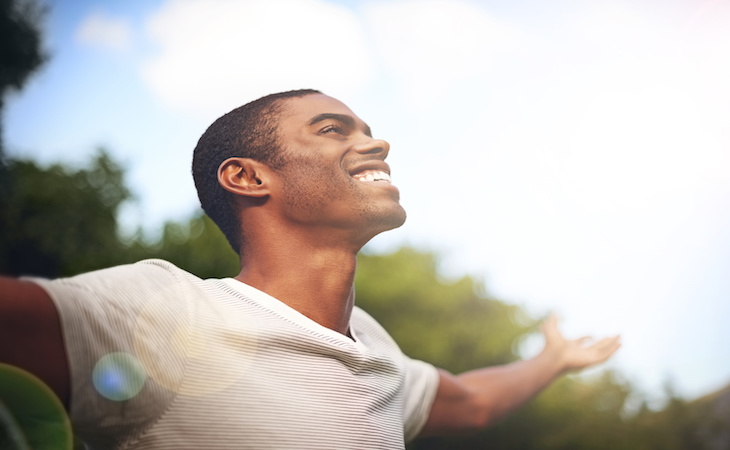 Shot of a man standing outside with his arms outstretched in sunlight